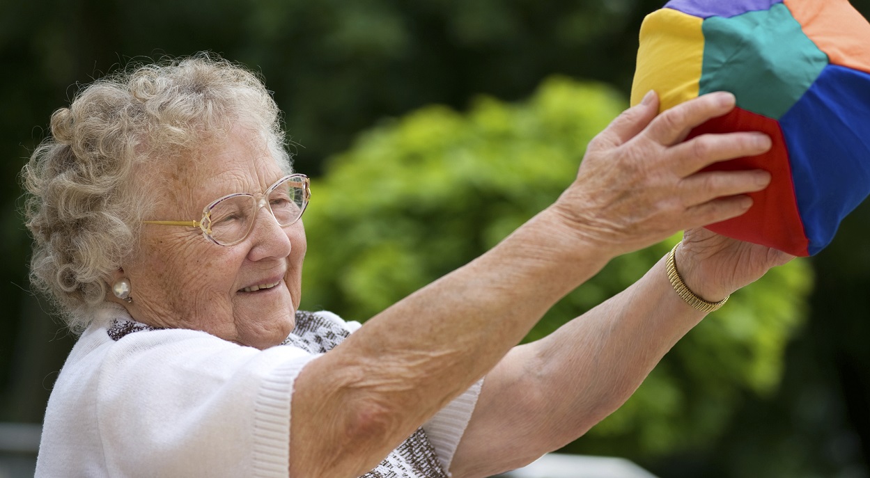 Seniorin hält Ball in den Händen und streckt Arme aus 
