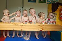 sieben Babys mit Trinkflaschen und Schnuller