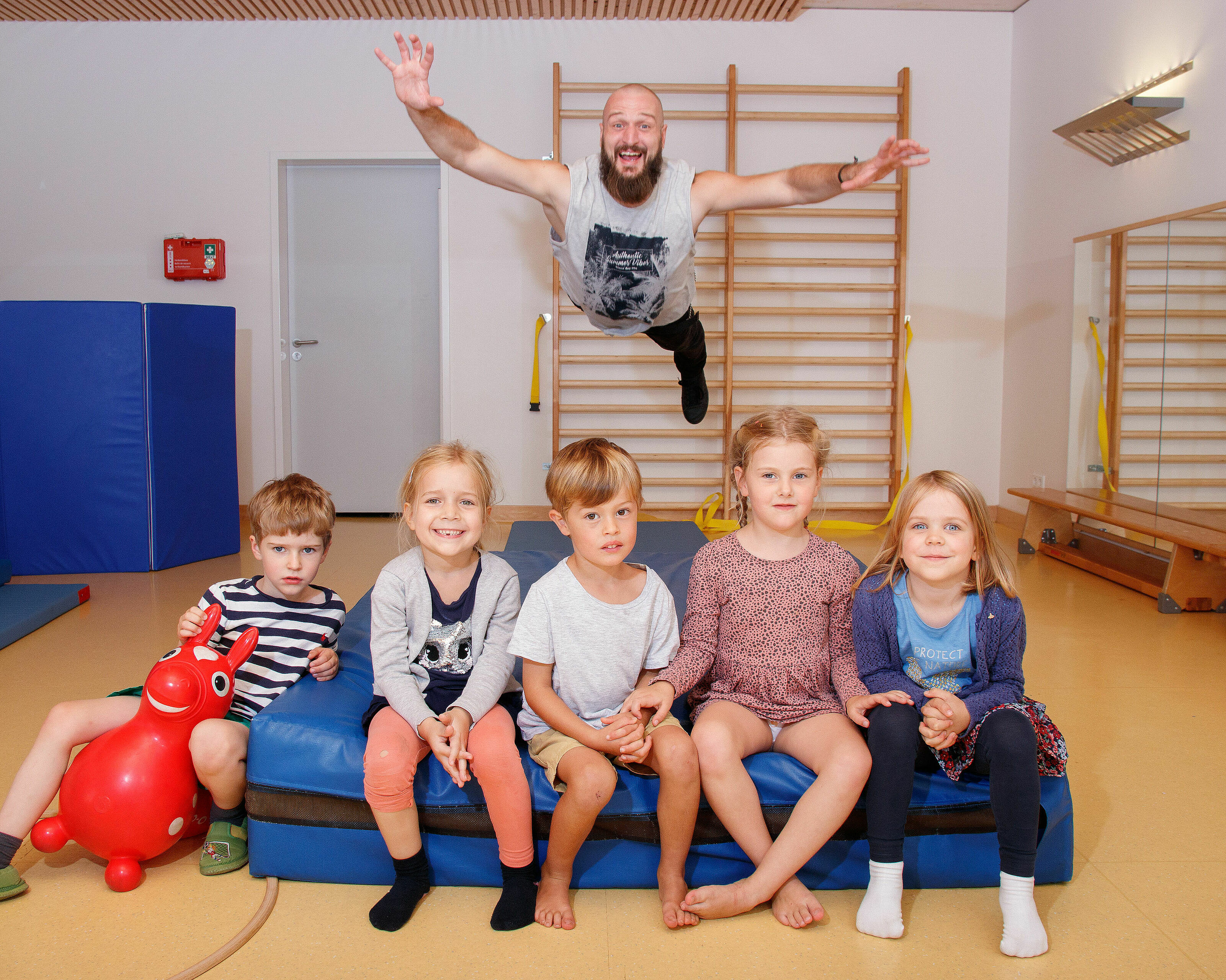 fünf Kinder auf Turnmatte mit Aufsichtsperson