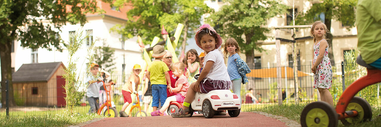 Kita Kindergarten Düsseldorf Symbolbild Andre Zelck Kinder auf Bobbycars im Kita Garten
