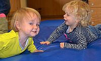 zwei lachende und krabbelnde Babys auf einer blauen Sportmatte