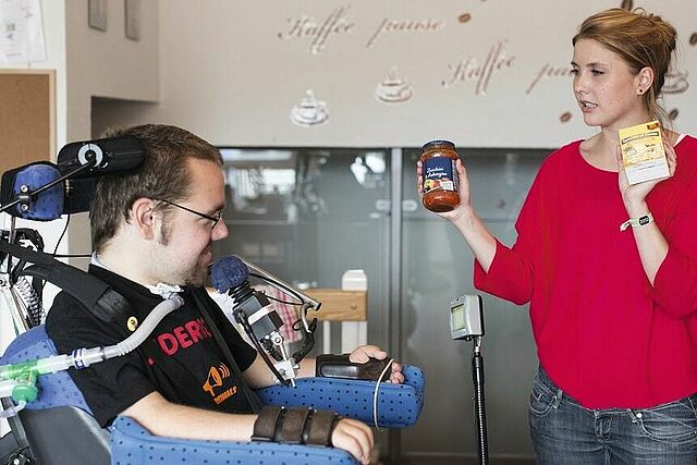 Frau unterhält sich mit zu pflegender Person im Rollstuhl